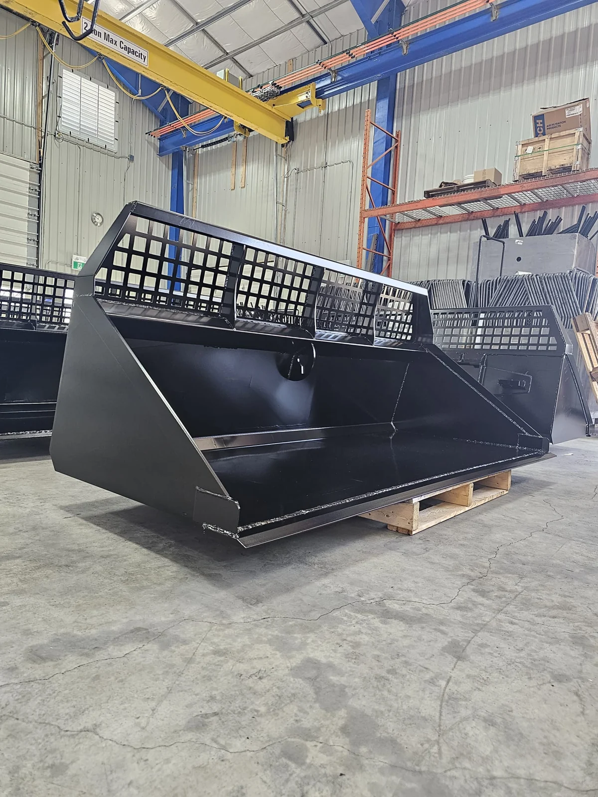 Black finished equipment buckets staged on a pallet indoors