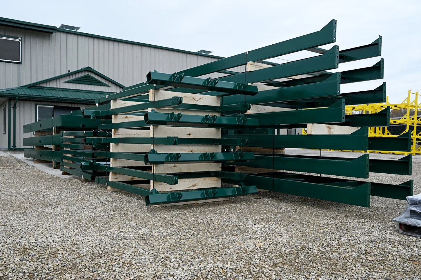 Green coated steel structures stacked on wooden spacers outside the facility